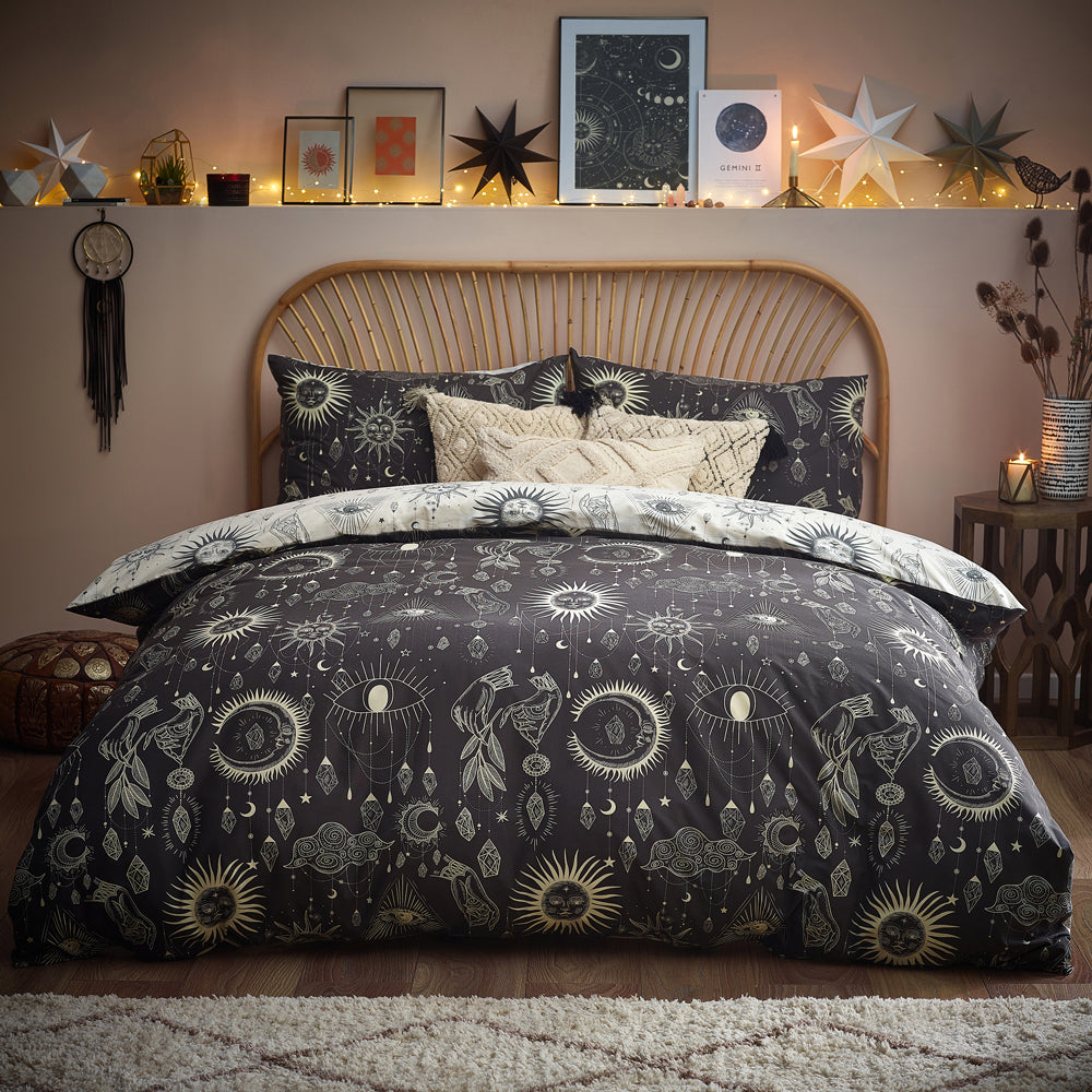 A bed with celestial-patterned bedding in a cozy room adorned with star-shaped lamps, framed pictures, and a dream catcher on a warm, lit backdrop.