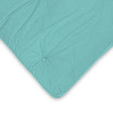 A teal cushion with a button in the center, resting on a white background with a slight wrinkle visible.