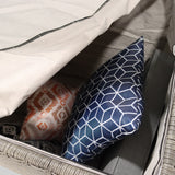 Decorative pillows are stored inside an open gray storage bin with a lifted white lid, partially revealing their patterns and colors.