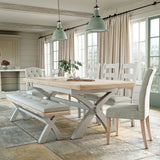 A wooden dining table set with chairs and a bench in a bright room, adorned with a vase of greenery, under hanging green pendant lights.