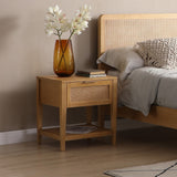 A wooden nightstand holds a vase with white flowers next to a bed with gray bedding. There's a beige wall and light wooden flooring for context.