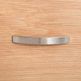 A curved metal handle is centered on a textured wooden surface, likely representing a piece of furniture or cabinetry.