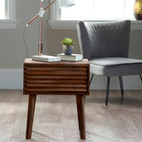 A wooden side table supports a metal lamp, books, and a potted succulent, situated near a window and a grey upholstered chair, in a well-lit room.