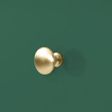 A gold-colored round door knob projects from a teal-colored wall, offering a simple, minimalist design element within a plain, unadorned context.