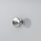 A brushed metal door knob is mounted on a plain light gray wall, casting a soft shadow.