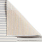 A corner of a layered, textured rug lifted to reveal its underside, highlighting the striped fabric and weave against a plain white background.