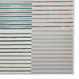 A patterned rug is displayed with alternating stripes in teal, brown, and shades of gray, creating a textured visual effect against a neutral background.