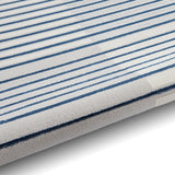 Striped textile, possibly a towel or fabric, with alternating light and dark blue stripes on a white background, resting on a flat surface.