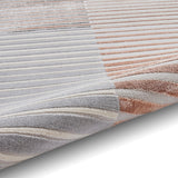 A striped rug with varying shades of gray, white, and rose lies flat, showcasing its texture and color gradient.