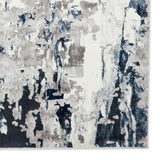 A textured rug with abstract gray, white, and navy brushstroke patterns creates a modern art-inspired appearance, seemingly displayed against a white backdrop.