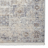 A textured rug features a distressed pattern in shades of beige, gray, and brown, with fringe on one edge.