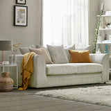 A striped sofa with pillows sits in a cozy living room, near a window with sheer curtains, accompanied by a side table, lamp, and decorative shelving.