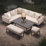 An L-shaped outdoor sectional sofa with cushions surrounds a central coffee table with a lamp. Additional seating includes a bench and a stool, set on a paved patio.