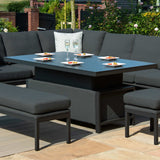 An outdoor dining set with dark cushions and a square table set for two sits on a patio, surrounded by a garden.