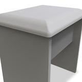 A grey upholstered ottoman with a square cushioned top and a sleek, simple base set against a white background. No visible action. The context is minimalistic.