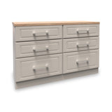 A wooden six-drawer dresser with a light brown top and silver handles sits idle in a white void.