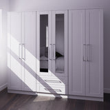 A large grey wardrobe with mirrored doors partially reflects the room, revealing a glimpse of a bed. Sunlight casts shadows across the floor and furniture.