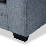 A close-up of a blue fabric sofa corner with a small black leg visible, against a light background.