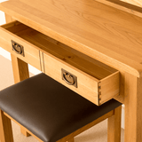 A wooden desk with an open drawer revealing dovetail joints, situated above a brown leather chair, in a warmly lit room.