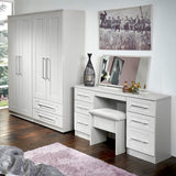 A white wardrobe and vanity furniture set stands in a room with wooden flooring, accompanied by decorative items and a large photograph on the wall.