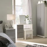 A serene bedroom space with a dressing table and mirror, flanked by a wardrobe and a bedside drawer with a lamp. A window with sheer curtains brightens the room.