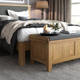 Wooden chest at the foot of a neatly made bed with soft bedding, in a cozy bedroom with neutral tones. A tray with a candle and plant rests atop the chest.