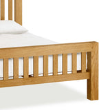 A wooden bed with a white pillow and bedding, set against a white background.