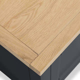 A light wooden tabletop corner sits atop a dark base, depicting a contrast between the wood texture and the base's solid color.