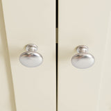 Two silver rounded knobs on a cream-colored cabinet door, positioned close to each other at the center where the doors meet.