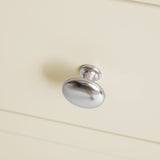 A silver drawer knob is attached to a cream-colored cabinet, with focus on the hardware against a soft background.