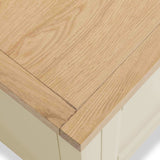 Wooden tabletop corner with a visible grain pattern, overhanging a cream-colored base or cabinet, viewed from a slightly elevated angle.