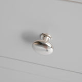 A silver, metal drawer knob protrudes from a white, flat surface, casting a soft shadow, signifying an interior design element.