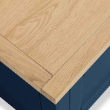 A light wood tabletop corner with visible grain rests above a blue structure, possibly a table or cabinet element, in a close-up view.