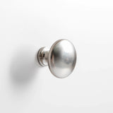 A round, silver door knob is mounted on a white door, positioned in the center of the image with a smooth background.