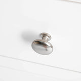 A silver, round cabinet knob is attached to a white, horizontal drawer front.