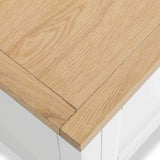 A wooden table corner with fine grain texture, overhanging a blurred white surface or space.