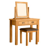 A wooden vanity table with an upright mirror and two drawers, accompanied by a matching stool with a brown cushion, isolated on a white background.