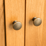 Two round, bronze cabinet knobs are attached to a wooden cabinet, positioned close together on adjacent doors.