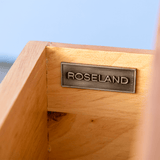 A metal plaque with the inscription "ROSELAND" is mounted on a wooden surface. The background is blurred with a hint of blue sky.