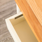 An open, empty drawer with a metal handle, partially obscured by a wooden tabletop. The surrounding floor has a grey wood grain texture.