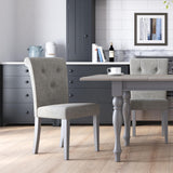 Elegant dining chairs flank a classic gray wooden table; a neat kitchen with cabinets and decor forms the backdrop. A serene atmosphere is suggested by the tidy, modern arrangement.