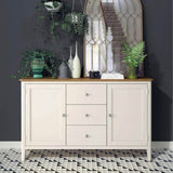 A light-colored wooden sideboard with decor, including vases and plants, against a grey wall with a geometric mirror, standing on a black and white patterned floor.