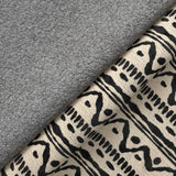 A grey plush towel lies atop a patterned fabric with geometric designs in black and beige, showcasing textures and home decor items.