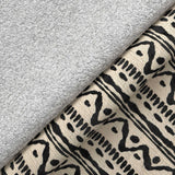 A gray plush towel rests on patterned fabric with abstract black designs, creating a contrast of textures.