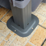 A gray plastic patio umbrella base supports a dark pole with a blue fabric element, set on a textured beige and orange tile surface.