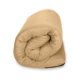 A beige bean bag chair is placed against a white background, with a deep crease at its center suggesting a soft and malleable structure.