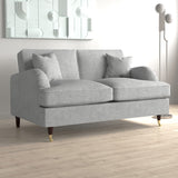 A grey, fabric chaise sofa with cushions is positioned in an interior setting, with light wood flooring and abstract wall art in the background.