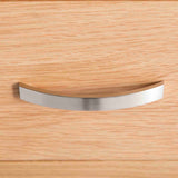 A silver, curved cabinet handle is attached to a wooden surface with a visible grain pattern, positioned centrally and viewed close-up.