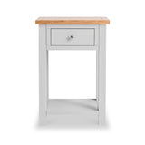 A white bedside table with a single gray drawer and a natural wood top stands idle against a plain white background.