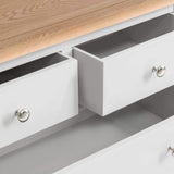 A white wooden dresser with open drawers revealing empty interiors, sporting round metal handles, against a minimalist background.